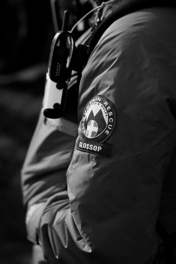 Person wearing a mountain rescue jacket with a visible patch on a dark background