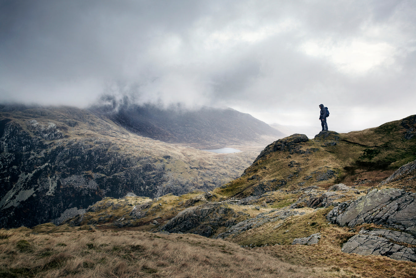 Person standing on a rocky outcrop overlooking a mountainous landscape with clouds.
