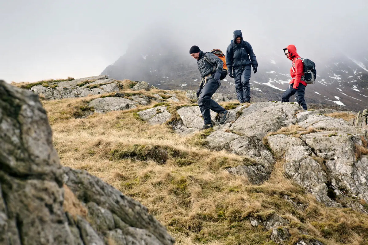 Three hikers on a rocky mountain path with foggy mountains in the background