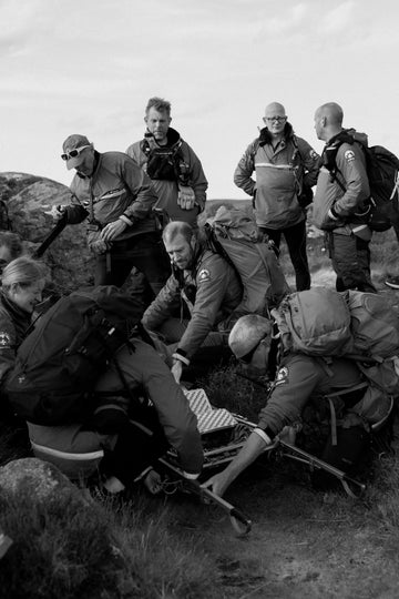 Rescue team in buffalo systems outdoor gear gathered around a person on a stretcher in a rocky landscape.