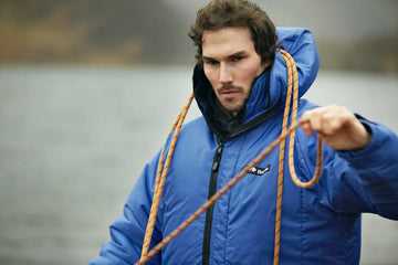 Man in a blue jacket holding a rope by a body of water