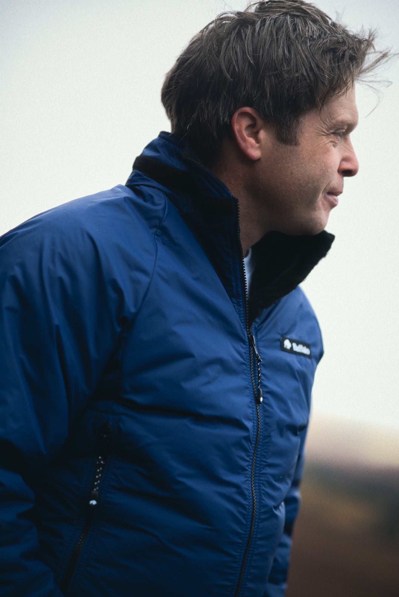 Man wearing a blue jacket with a brand logo on a blurred background