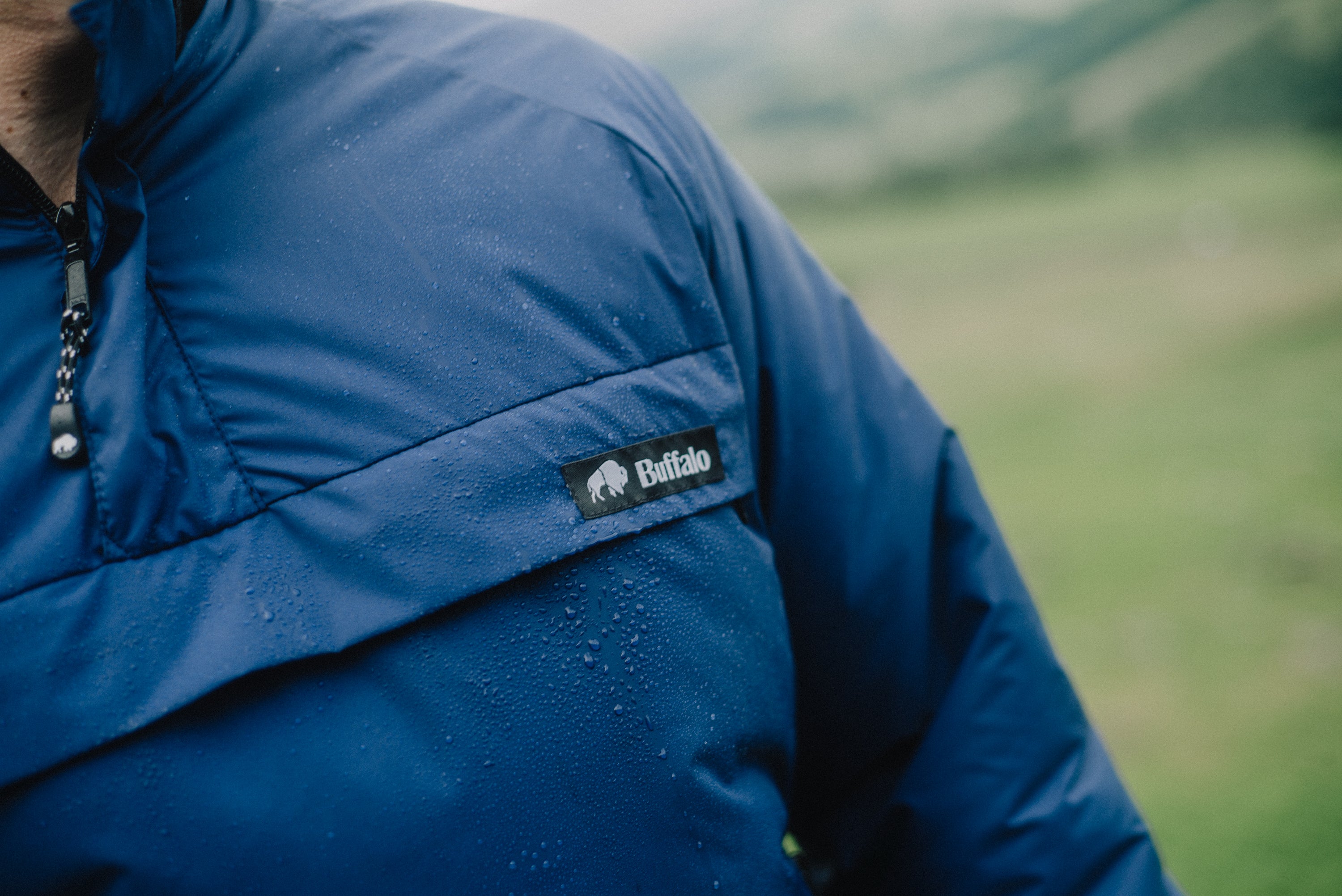 Close-up of a blue jacket with a brand logo against a blurred natural background