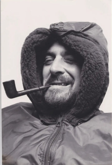Black and white photo of a person wearing a fur-lined hood with a pipe in their mouth.