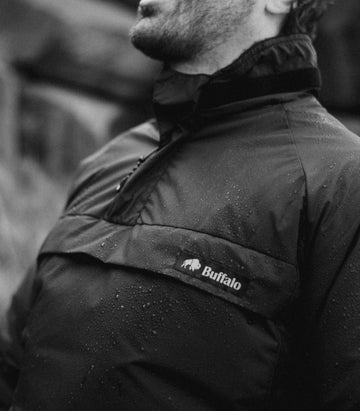 Person wearing a black jacket with a visible buffalo systems logo in a blurred outdoor setting